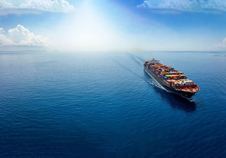 A wide shot of a cargo vessel sailing calm seas that stretch to the horizon, where it blends into the blue sky