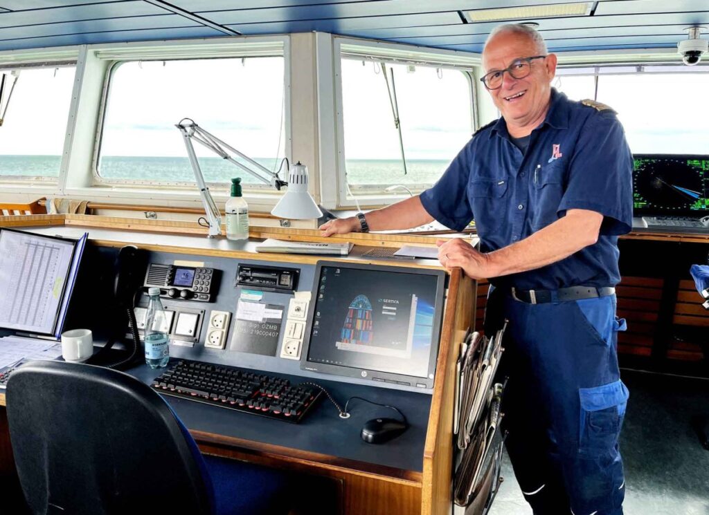 A picture of Allan Hjortnæs Pedersen, Chief of Maintenance at Læsøfærgen, standing on the bridge of the vessel, next to the control desk