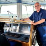 A picture of Allan Hjortnæs Pedersen, Chief of Maintenance at Læsøfærgen, standing on the bridge of the vessel, next to the control desk