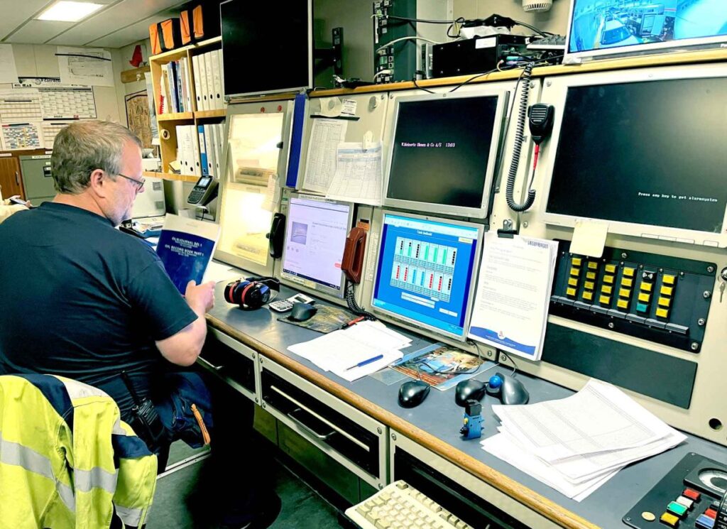 A picture of a maritime worker at Læsøfærgen sitting at a desk, surrounded by multiple screens displaying various data and controls