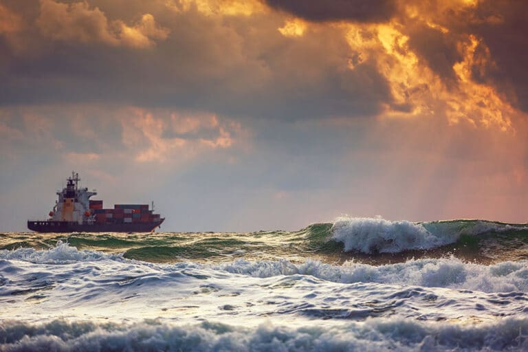 A cargo ship at sea in the distance with rows of colorful shipping containers