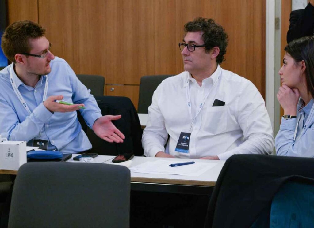 Three DFDS employees engaged in a discussion, sitting at a desk at a conference