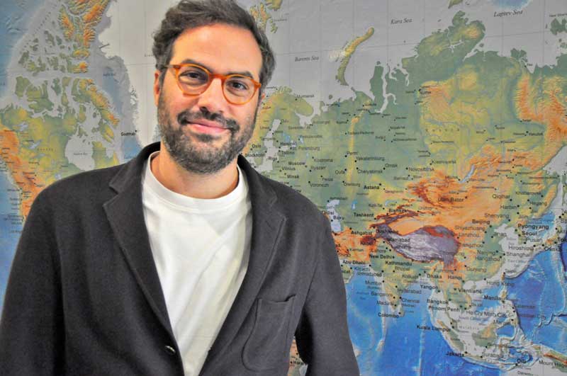 A portrait of Project Manager Salonikos Salonikidis of SEAMAR standing confidently in front of a large world map