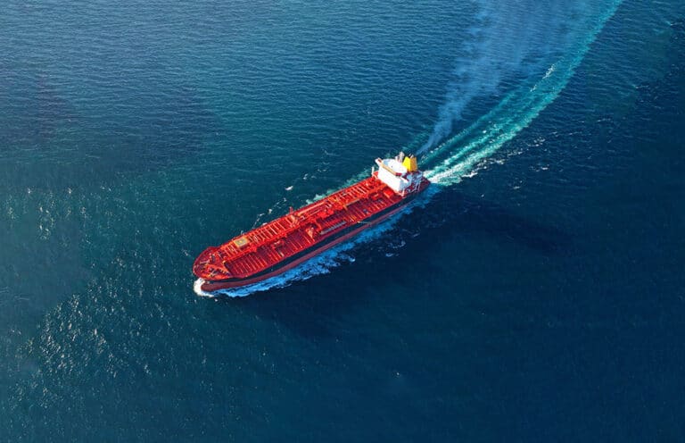 An overview of a tanker vessel at sea, sailing at full speed across the frame