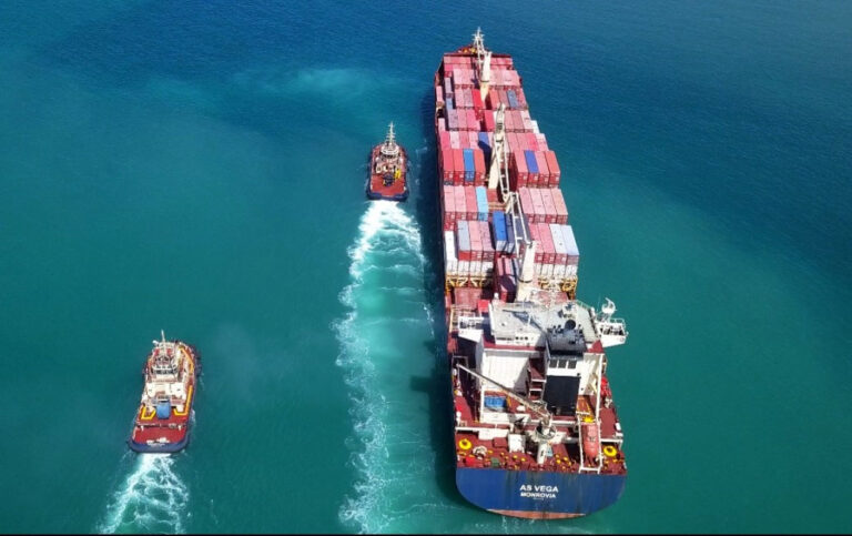 An overview of a large tanker vessel accompanied by two tugboats, all sailing smoothly across calm seas