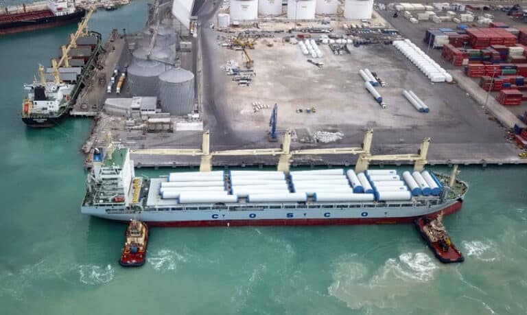 A photo of a maritime vessel being guided into dock by two tugboats, assisting with precise maneuvering in the harbor