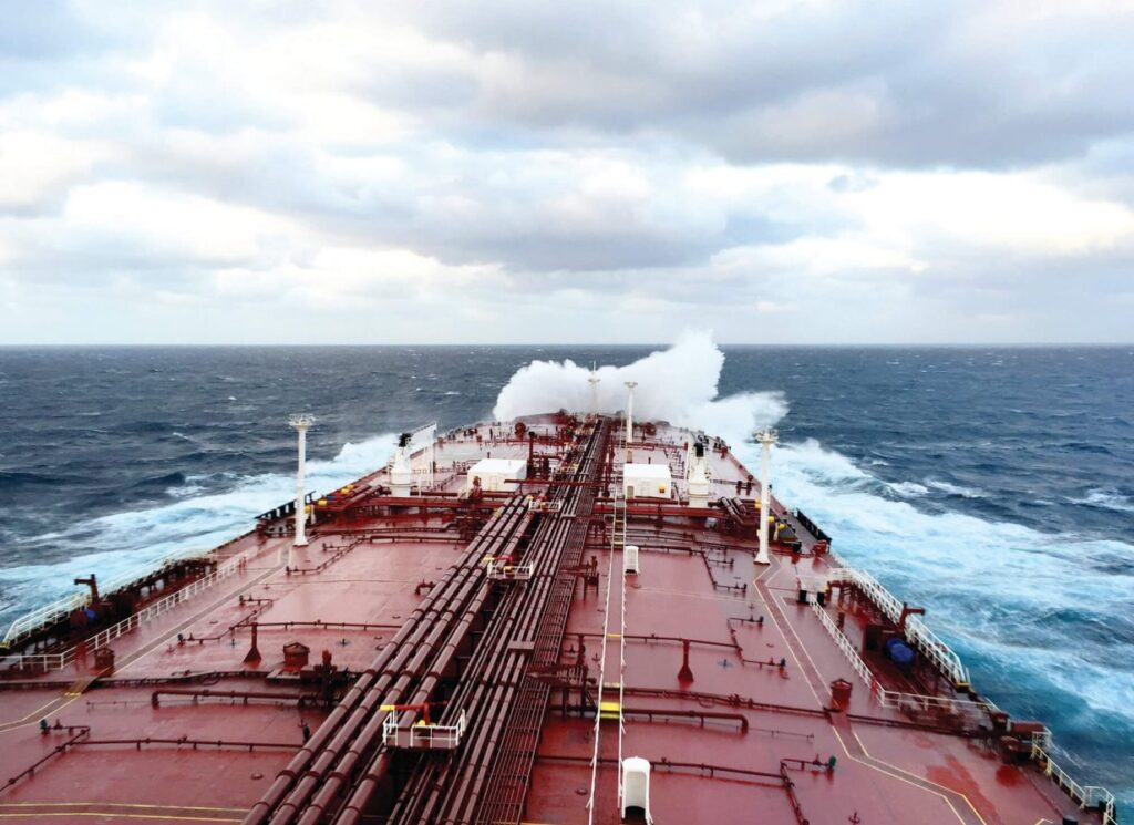 A close-up view of a tanker ship's deck sailing through dynamic waves on the open sea