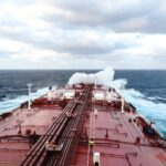 A close-up view of a tanker ship's deck sailing through dynamic waves on the open sea