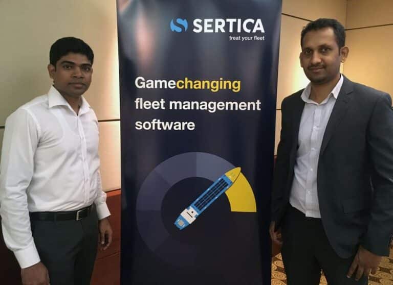 A group photo of the two new employees at the Singapore department for SERTICA, standing side by side next to a roll-up banner featuring SERTICA graphics