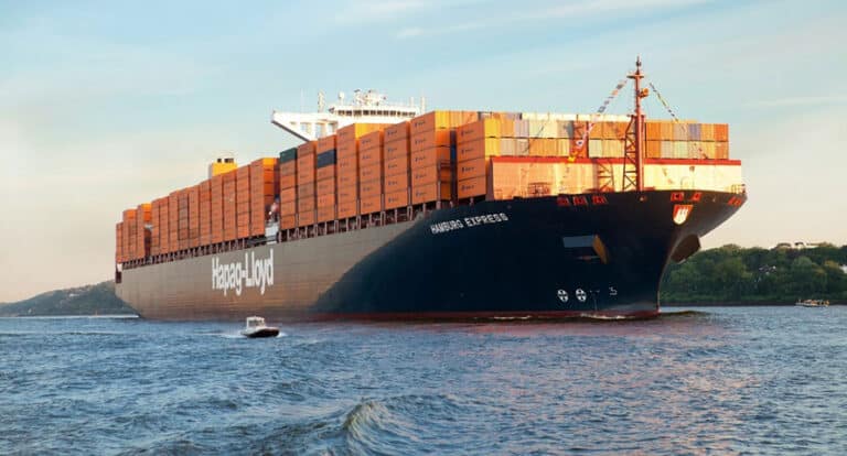 A large black cargo ship with neatly stacked multicolored containers on its deck, being carefully guided through the water by a tugboat assisting with navigation
