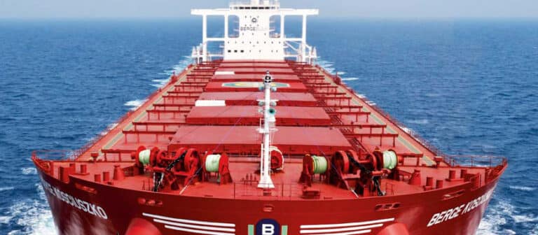 A close-up of the bow of a large red maritime vessel, gradually expanding down the deck and leading up to the tower