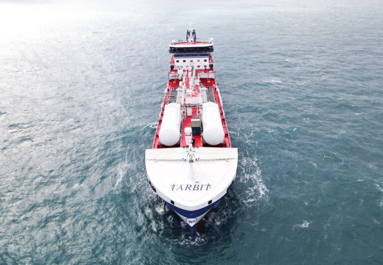A bird's-eye view of the TARBIT maritime vessel navigating the open sea, with the perspective coming from the front of the ship
