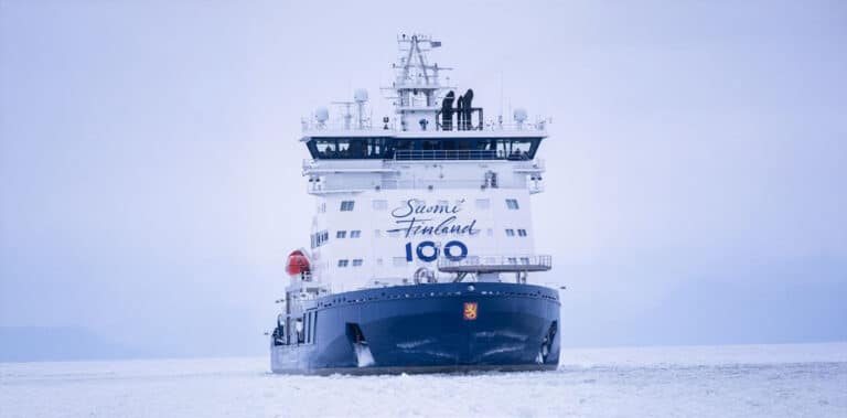 A front view of an icebreaker vessel at sea, powerfully cutting through thick ice with its reinforced hull